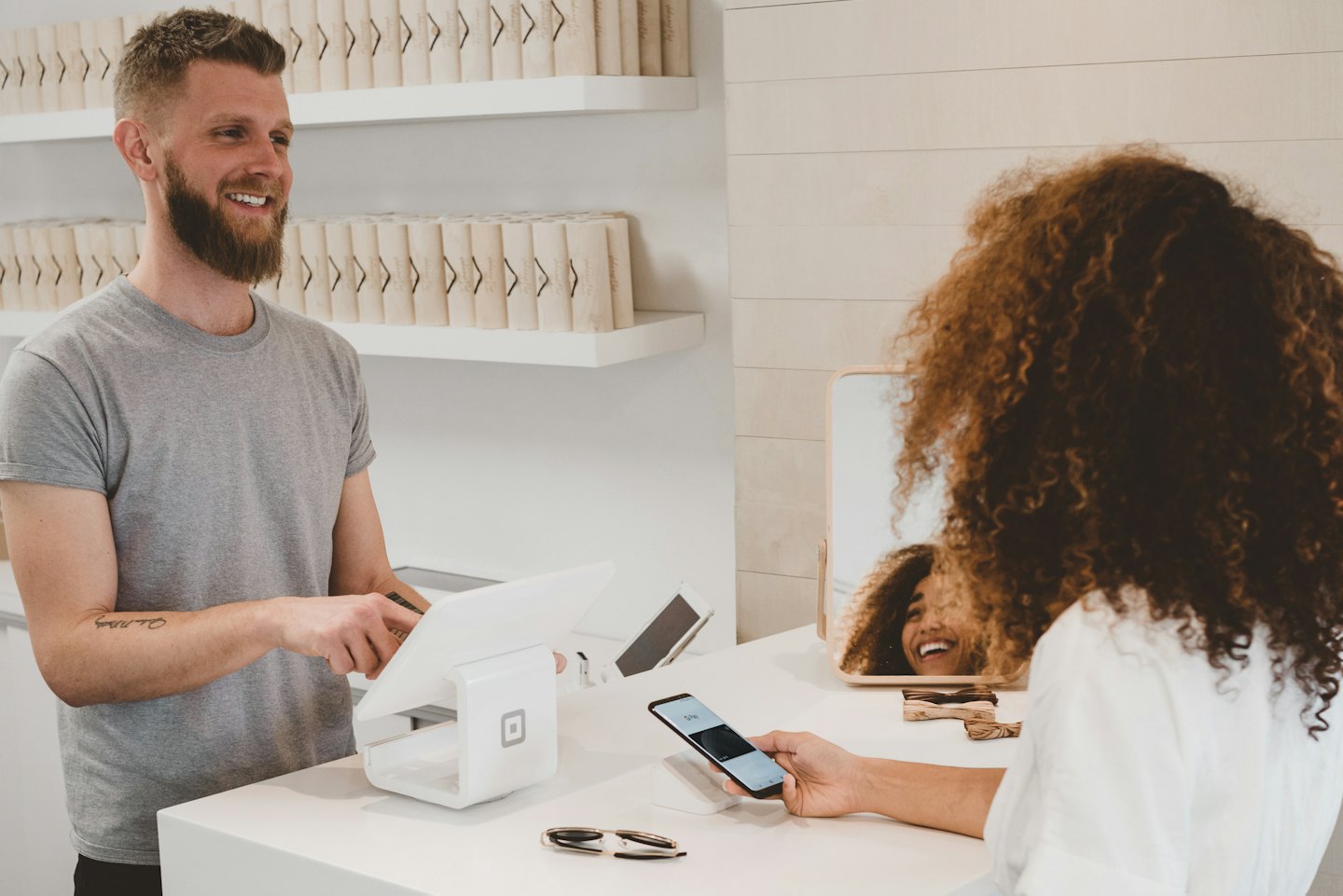Salesperson helps customer pay with phone at counter.