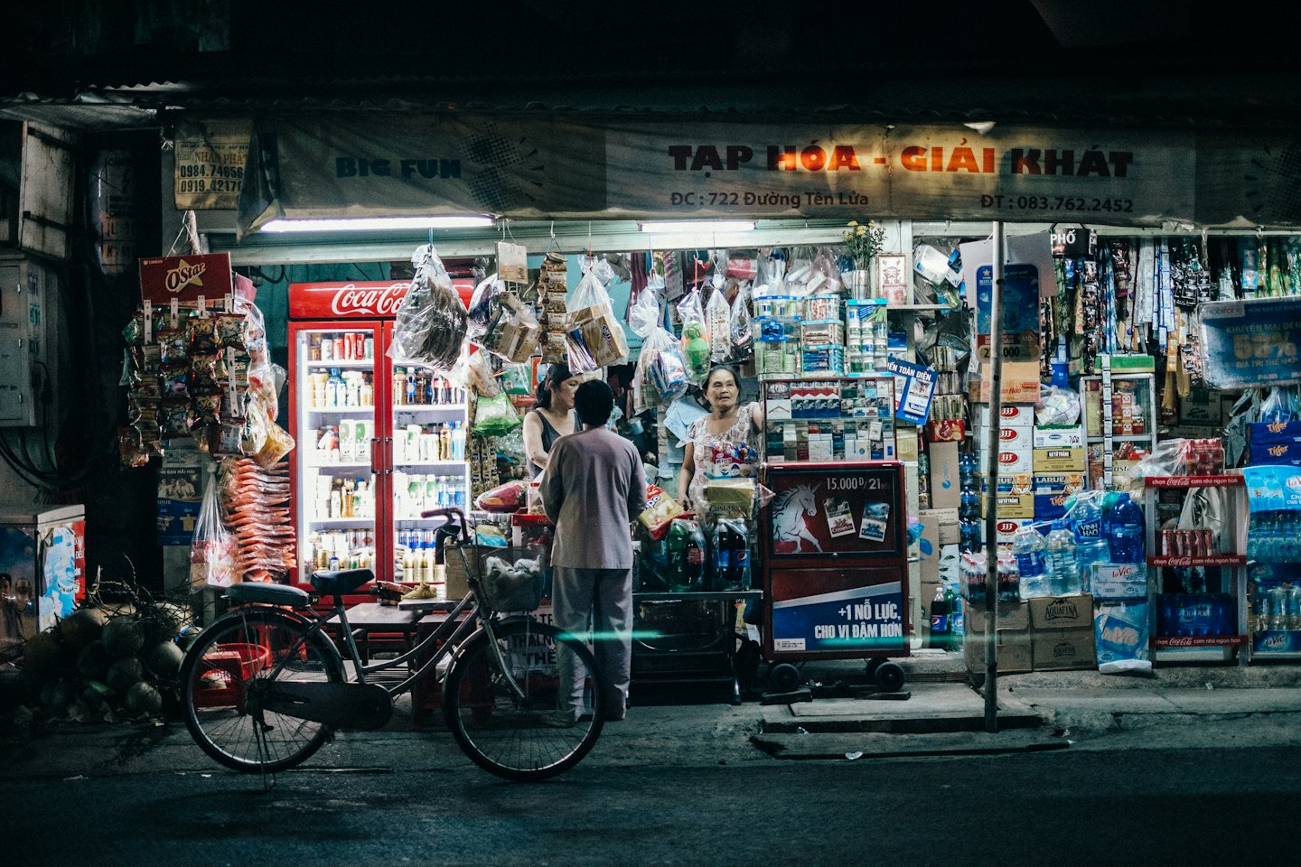 A smiling vendor stands in a brightly lit convenience store at night.